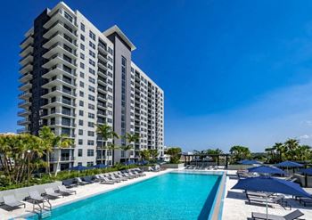A swimming pool with chaise lounge chairs and umbrellas in front of a tall building